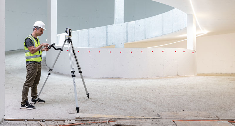 Leica iCON iCS20 gemotoriseerde bouwtool gebruikt door werknemer in een veiligheidsvest om een gebogen betonnen muur te meten.